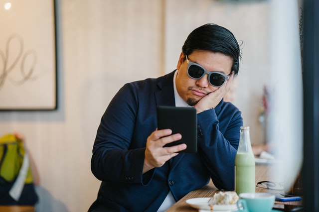 Znudený muž v slenčných okuliaroch a modrom obleku pozerá do tabletu.jpg
