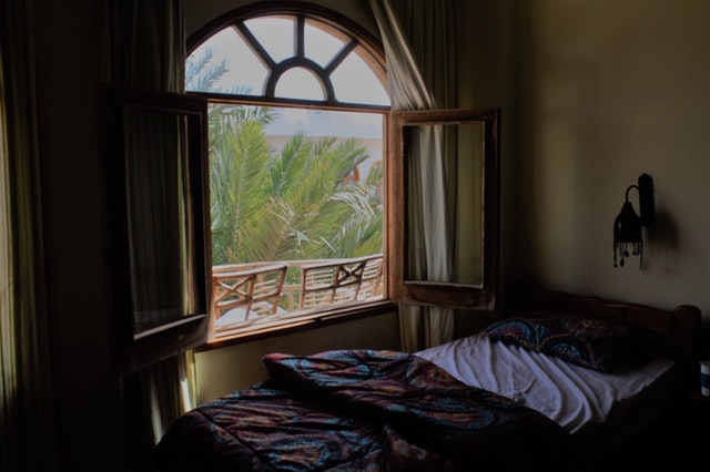 Posteľ s farebnými obliečkami pod oknom s drevenými okenicami